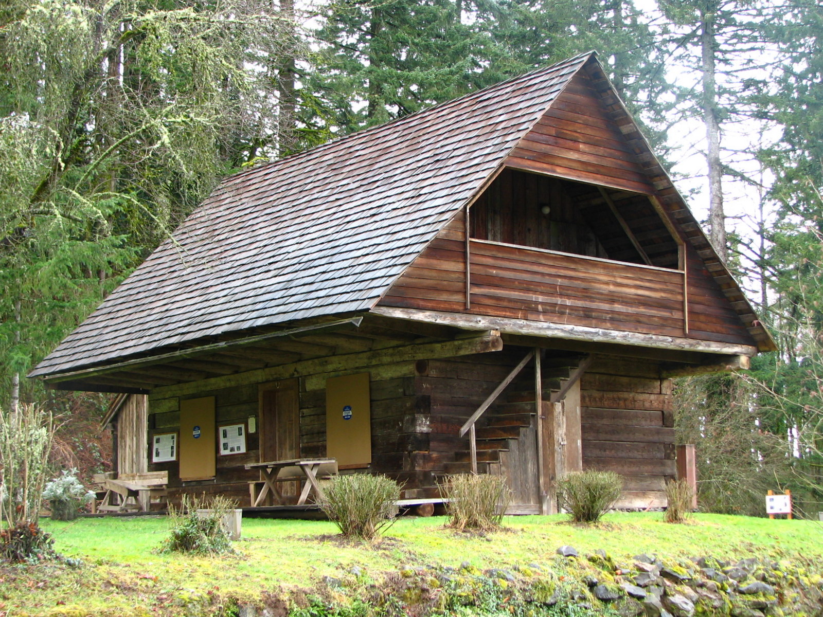 Photograph of a two-story log cabin, with an extreme overhang of the second